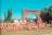 A variety of clay pots and vases are neatly arranged on the ground in front of an old stone archway. The arch is part of a larger stone wall, and there are trees and shrubs growing nearby. The sky is clear and bright blue, contributing to a serene atmosphere.