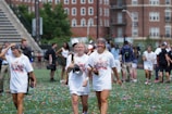 A group of young women, wearing 'National Champions' t-shirts, walk across a field covered with colorful confetti. They appear to be celebrating a victory. The background shows a few people mingling and large brick buildings.