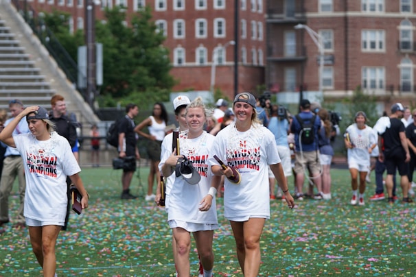 Young university athletes wearing colorful sport-themed hoodies, smiling and celebrating together outdoors.