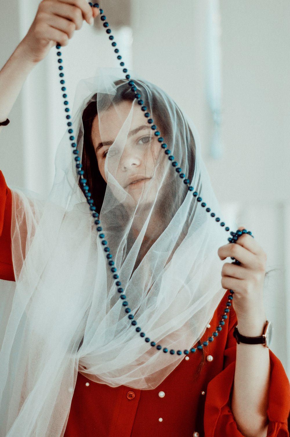 woman wearing white headdress and red dress holding black beaded necklace