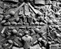 A complex arrangement of various sports equipment and attire, including tennis rackets, soccer balls, basketballs, helmets, shoes, gloves, and a mannequin torso wearing a T-shirt. The items are layered and artistically displayed in a monochrome color scheme, creating an intricate texture and visual pattern.
