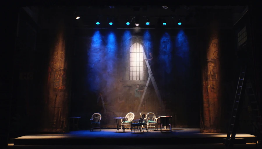 An intimate stage set with chairs under blue spotlights, ready for a community event