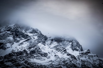 Snow-covered mountains are partially obscured by clouds, with a cable car traversing through the misty atmosphere.