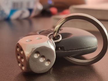 A metallic die keychain attached to a black car key lies on a dark surface, with a blurred background.