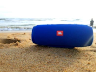 A compact, portable Bluetooth speaker resting on a sandy beach at sunset.