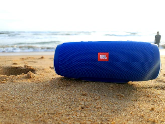 A rugged portable speaker splashing water at a beach party under sunset skies.