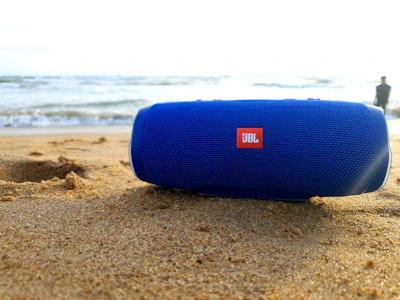 A sleek wireless speaker resting on a sandy beach with ocean waves in the background