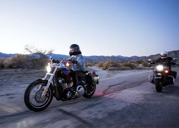 Motorcyclists riding together on a scenic road at sunset with blue and black tones.