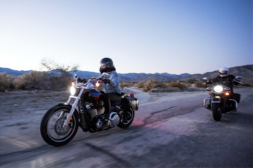 Motorcyclists riding across the rugged Moroccan Atlas Mountains at sunset.