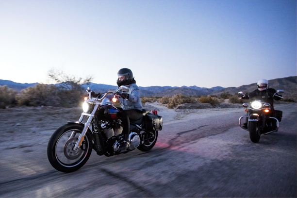 Motorcyclists riding together on a scenic road at sunset with blue and black tones.