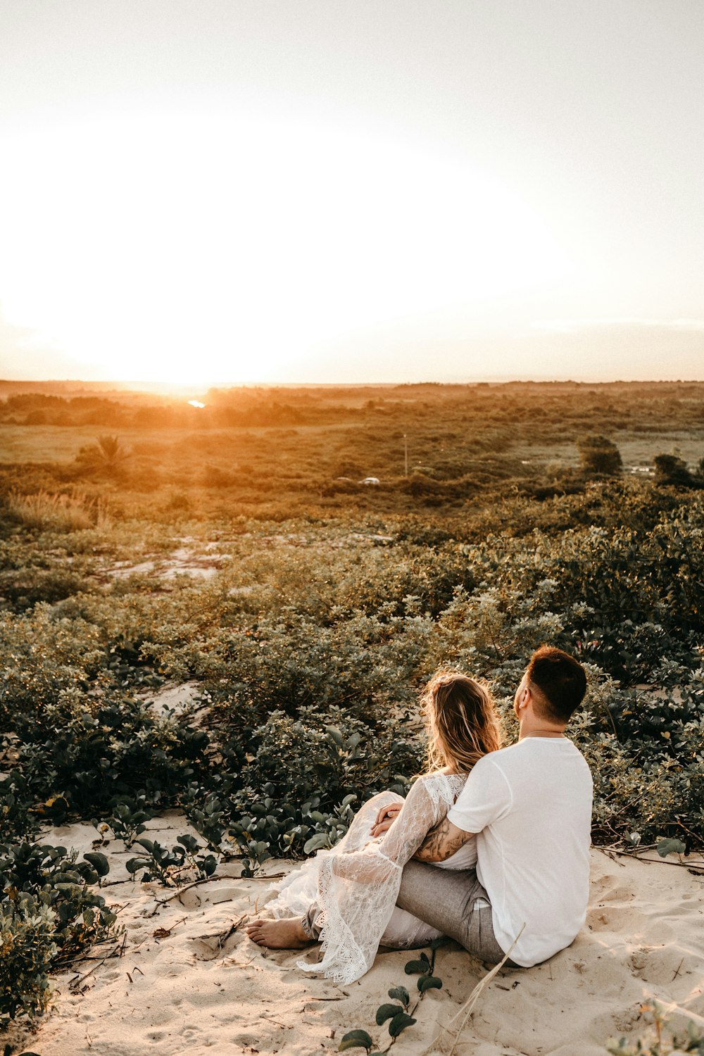 man and woman sitting on sand surrounded by flowers