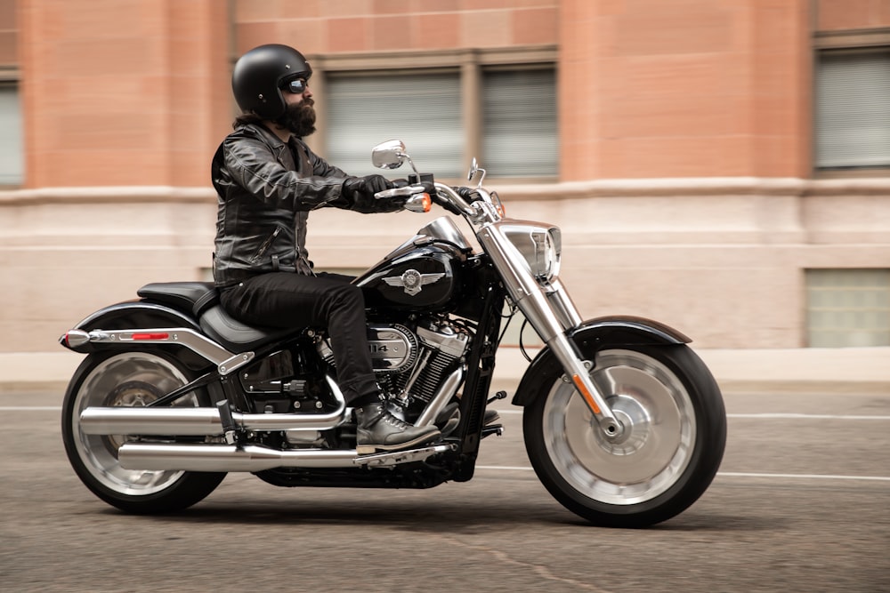Mann fährt schwarz-graues Motorrad auf asphaltierter Straße in der Nähe eines braunen Betongebäudes