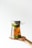 A hand holding a large glass jar filled with a liquid and sliced green fruits. The jar is topped with a metal lid and covered with plastic wrap.