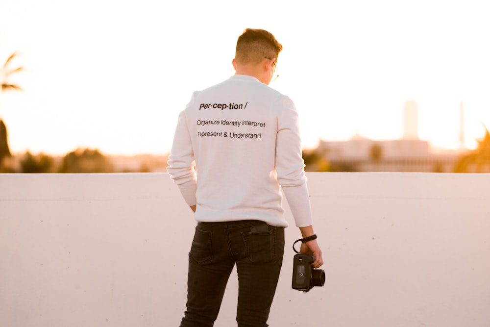 man in white top and black pants holding camera