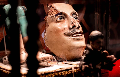 Close-up of a twisted papier-mâché mask with cracked textures and haunting eyes.
