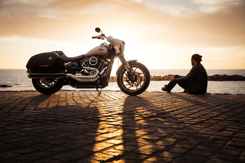 Mann sitzt auf dem Boden neben geparktem silbernem Cruiser-Motorrad