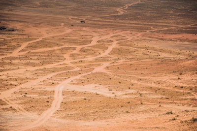 A drone flying low over a sandy trail winding through the desert.