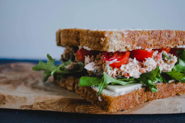 Close-up of a rustic, handmade sandwich filled with fresh ingredients on a wooden board.