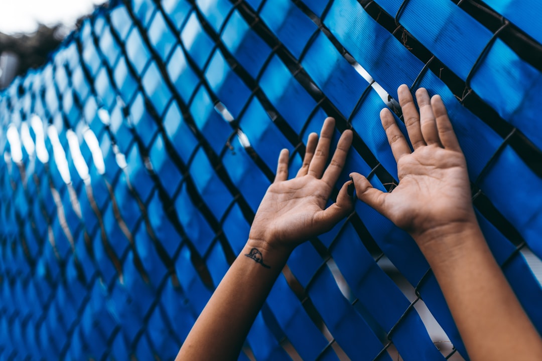 person raising their arms beside blue wall