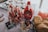 A table is set with an assortment of sweet treats, including lollipops in a glass container, a bottle of Hershey's syrup, wrapped candies, and a basket of chocolate chip cookies. There is also a tray of skewered snacks in the background.