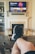 A person is relaxing in a living room with feet up on a wooden table. A TV mounted above a fireplace is displaying a popular streaming platform. Shelves on either side of the fireplace hold decorative items. A smartphone can be seen on the table.