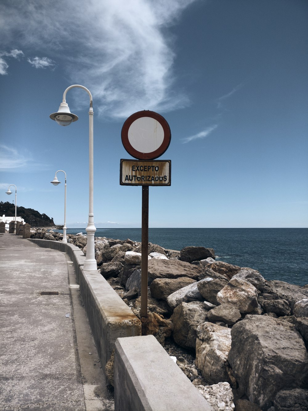 white and gray lamp post near rock formation on seashore viewing calm sea under white and blue skies