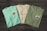 Three t-shirts are displayed on a dark wooden surface. The t-shirts have different prints, with the first one being light turquoise with the word 'Doheny', an orange fish graphic, and the text 'The Lagoon'. The second shirt is off-white featuring 'Starboard Creek' across the chest. The third t-shirt is olive green with the words 'La Jolla' and an image of a kayak with 'The Cove' written underneath.