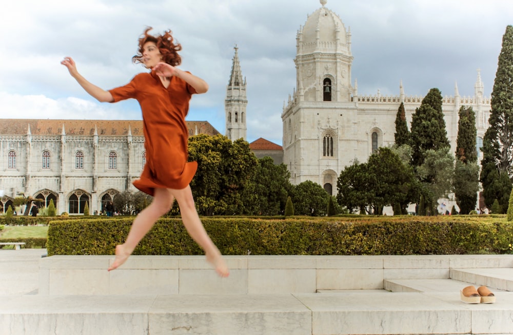 woman leaping off concrete pavement near dom building during daytime