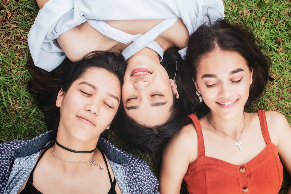 three women lying on grass with heads close to each other