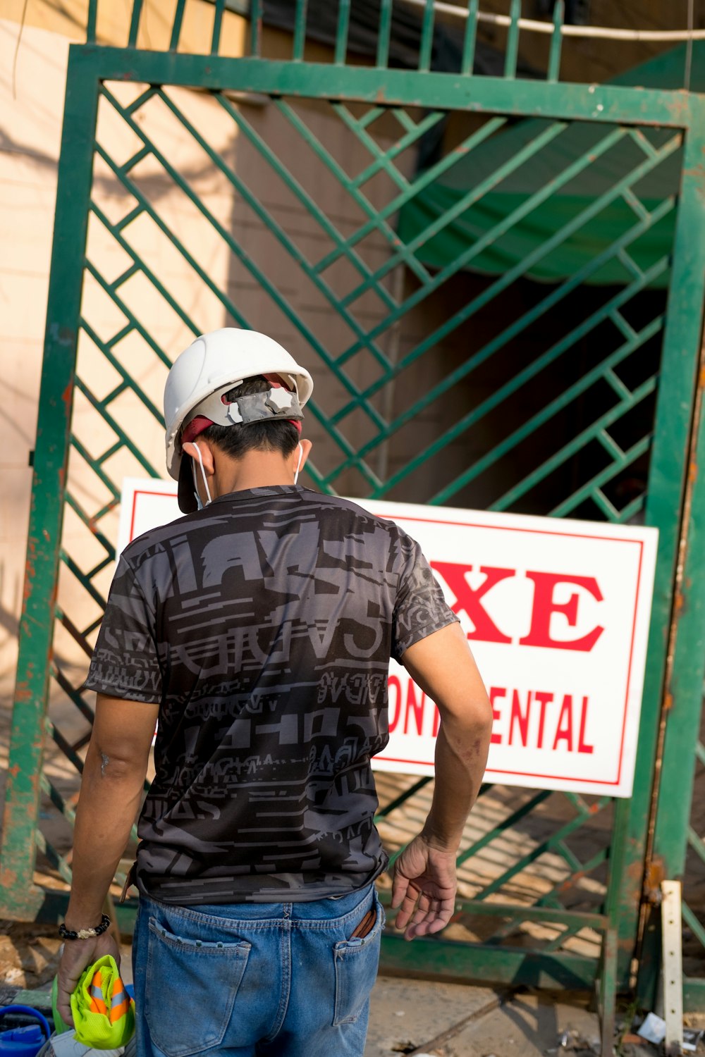 man wearing white hardhat walking towards green gate