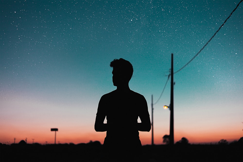 silhouette of person standing near utility pole during night