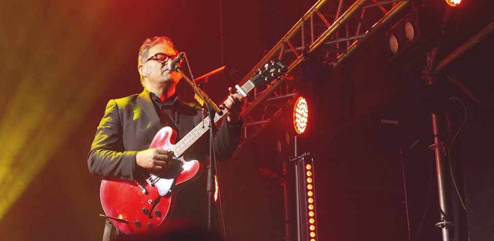 man standing and playing with red electric guitar in front of microphone