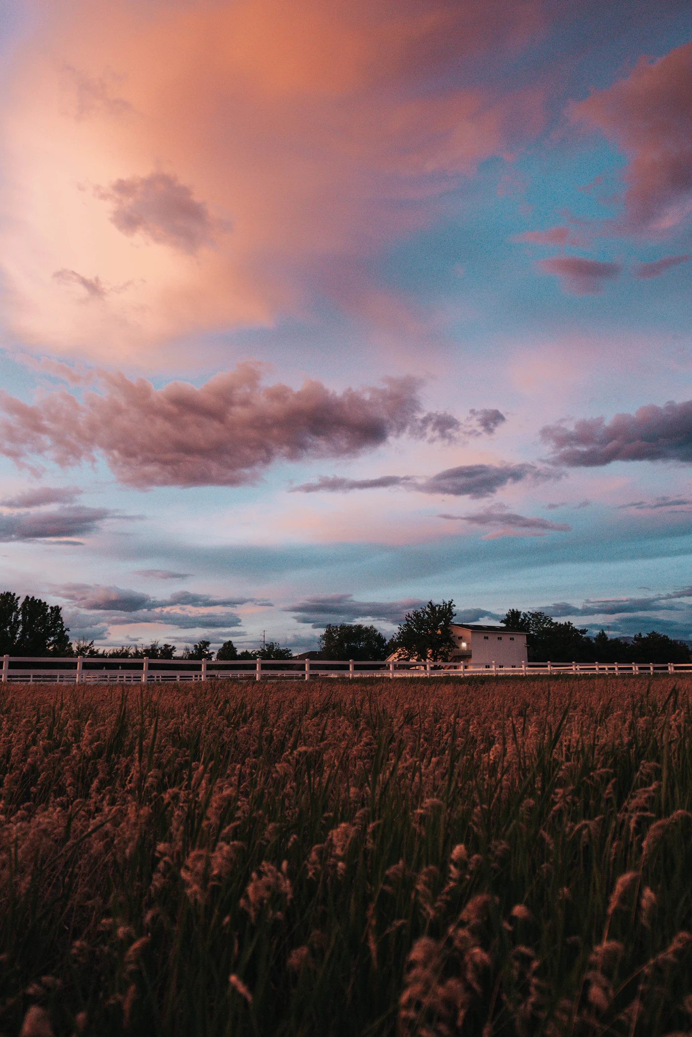 A farmhouse and green field under an orange and blue evening sky