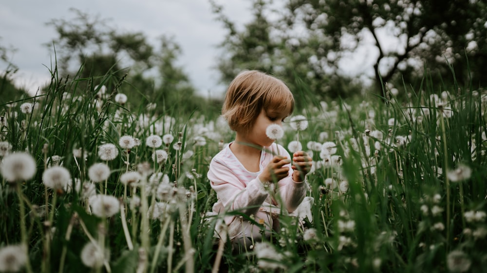 girl sitting on field of dandelions during day