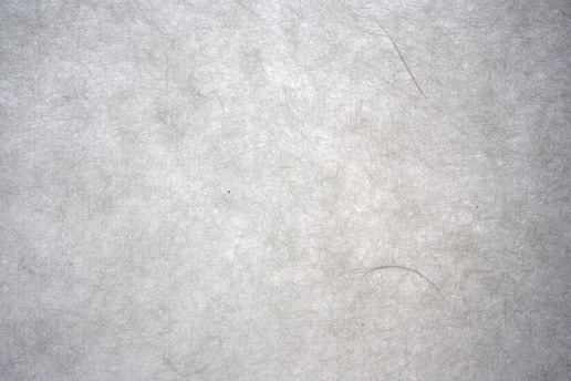 A textured surface with a fibrous, paper-like appearance. The material has a light gray tone with visible fibers and a slightly rough texture, giving it a natural and organic look.