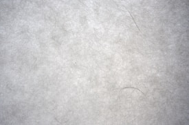 A textured surface with a fibrous, paper-like appearance. The material has a light gray tone with visible fibers and a slightly rough texture, giving it a natural and organic look.