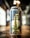 A can of beer is prominently displayed on a wooden surface, featuring a label with a gold illustration of a tower and a hop. Various colorful symbols resembling flags are scattered across the design. The background is blurred, with soft lighting creating a warm atmosphere.
