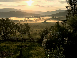 Sunrise over a green farmhouse with sprawling fields and morning mist