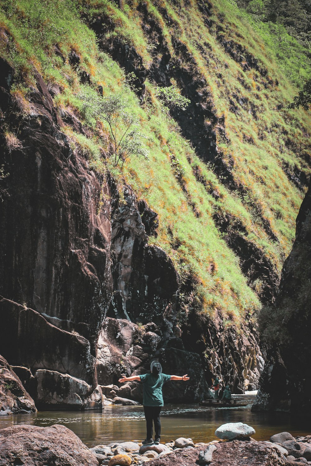 person standing on rock by the river with arms open