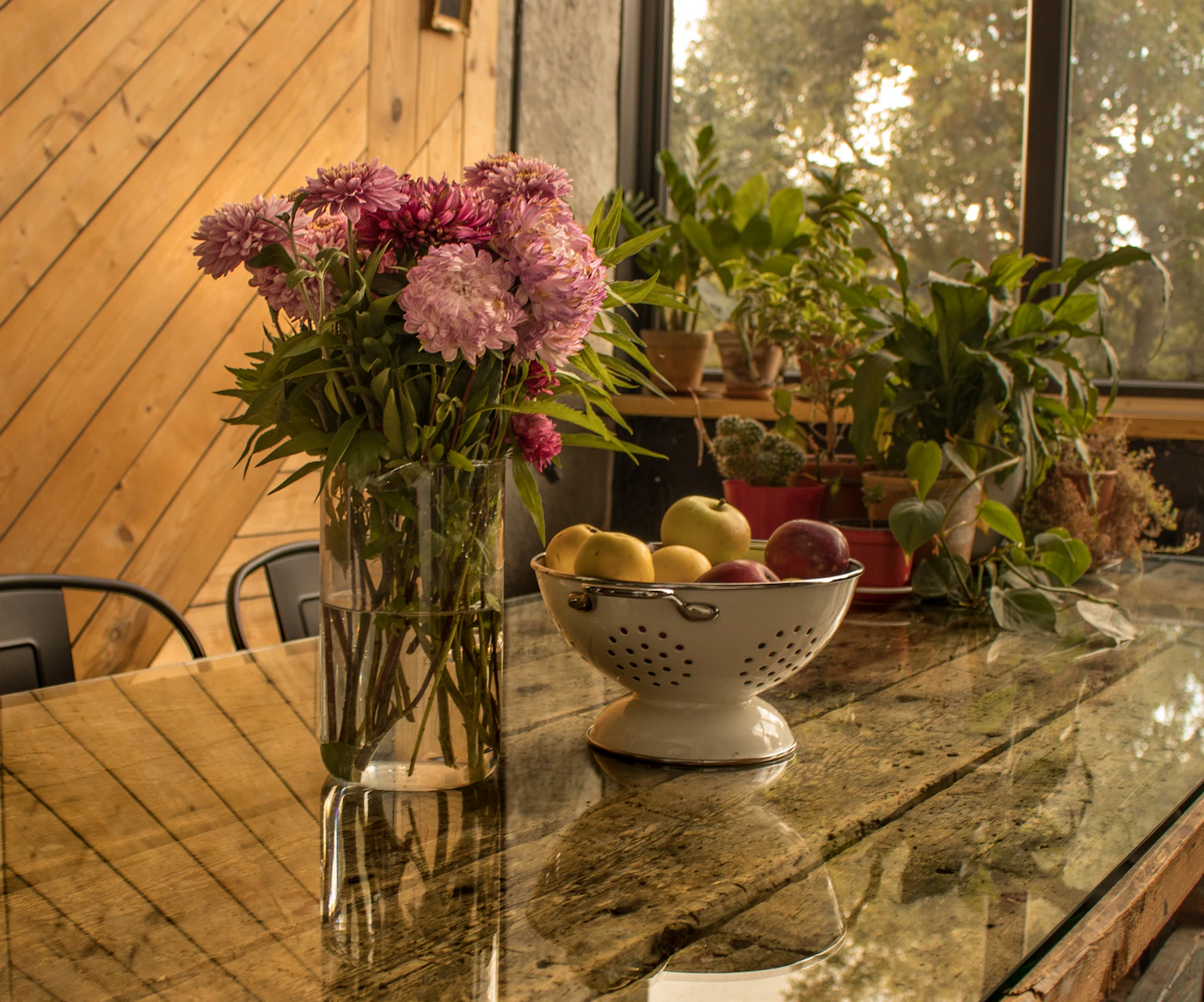 Fresh flowers and apples sharing the same wooden table near a window