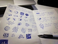 Close-up of hands sketching logo concepts on paper with pencils and markers.