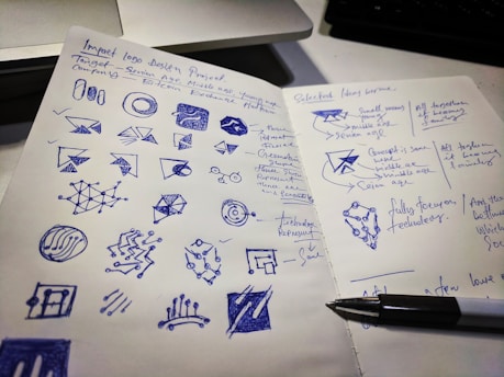 A designer sketching logo concepts on a notepad surrounded by color swatches.
