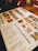 A restaurant menu placed on a wooden table, featuring images and prices of various dishes and drinks. The menu includes sections for starters, main courses, and beverages, with detailed photographs of each item. Items like baked goods, pasta, and drinks are highlighted.
