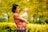 A woman in a red patterned shirt is holding a laughing baby outdoors surrounded by bright yellow and green foliage.