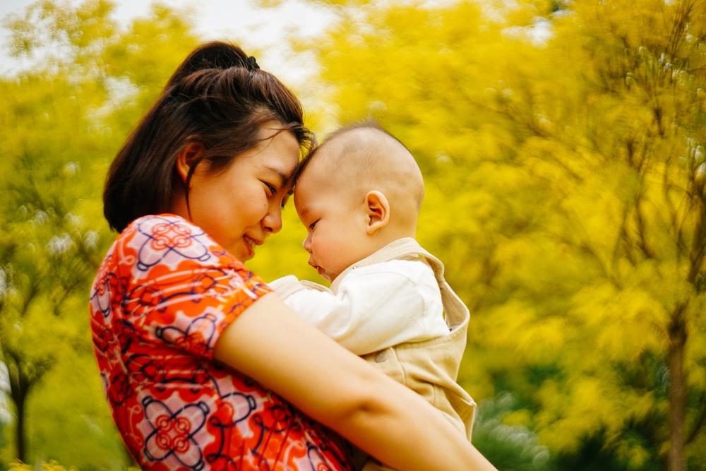 woman carrying baby near yellow trees