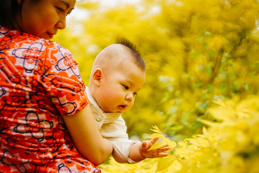 woman in orange, white, and black floral short-sleeved shirt holding baby