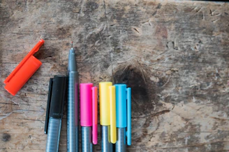 Close-up of smooth-writing pens in various colors resting on a wooden desk.