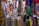 A colorful fabric store filled with various vibrant textiles. The fabrics are hanging and stacked all around, displaying an array of patterns and colors. Amongst the fabrics, a person is resting, lying down on a pile of materials, appearing relaxed amidst the bustling market environment.