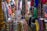 A colorful fabric store filled with various vibrant textiles. The fabrics are hanging and stacked all around, displaying an array of patterns and colors. Amongst the fabrics, a person is resting, lying down on a pile of materials, appearing relaxed amidst the bustling market environment.