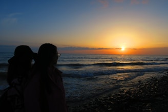 Two travelers sharing a sunset at a beautiful beach, smiling warmly.